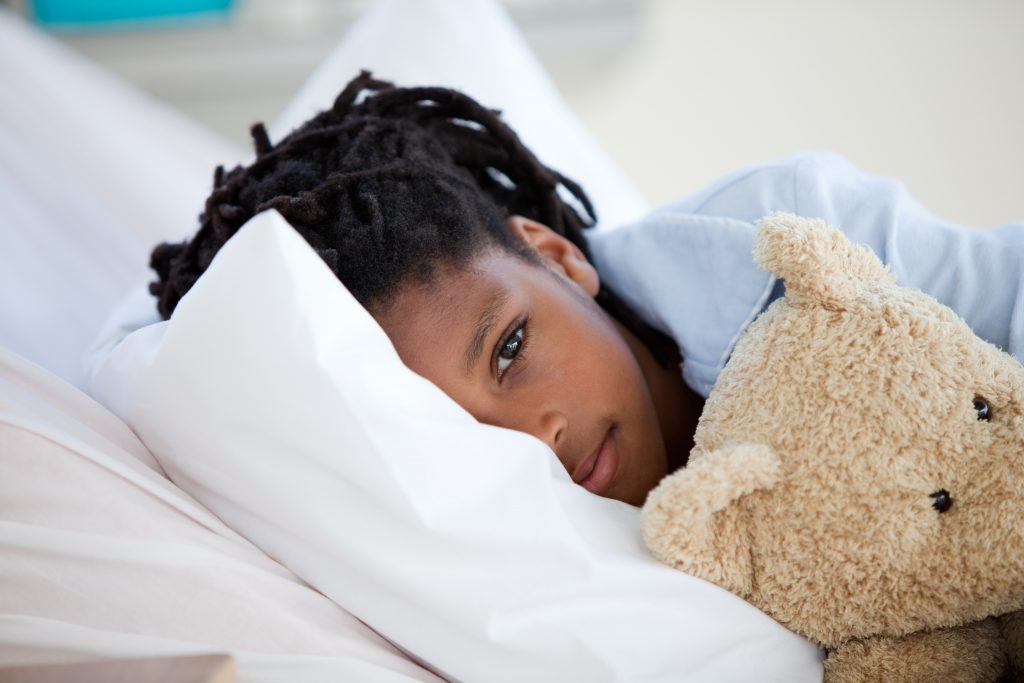 child laying in bed with teddy bear